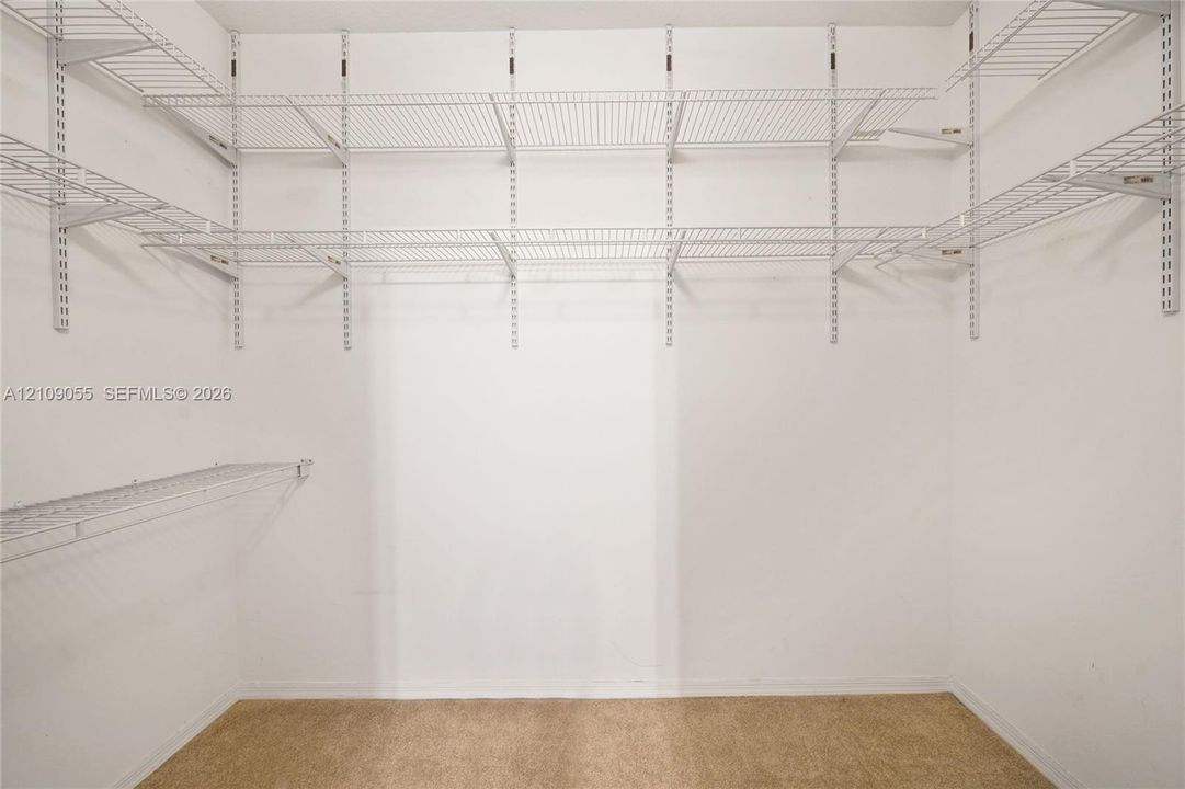 Storage area featuring white wall-mounted wire shelving systems and neutral-tone carpeting