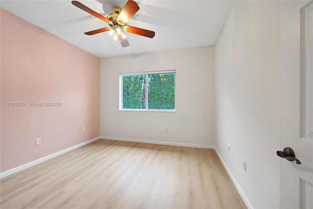Room featuring wood-finish flooring, a ceiling fan with integrated lighting, and a window with a natural exterior backdrop