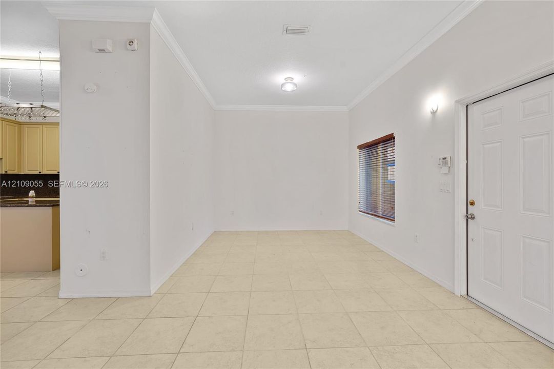 Neutral-toned tile flooring, crown molding, a multi-panel exterior door, and a recessed window with horizontal blinds
