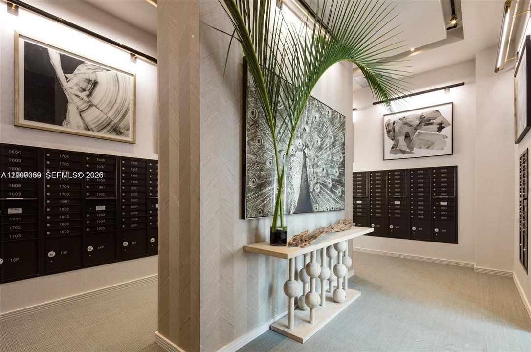 Mail room area featuring dark metallic parcel lockers, textured herringbone wall surfaces, track lighting, and a neutral color palette