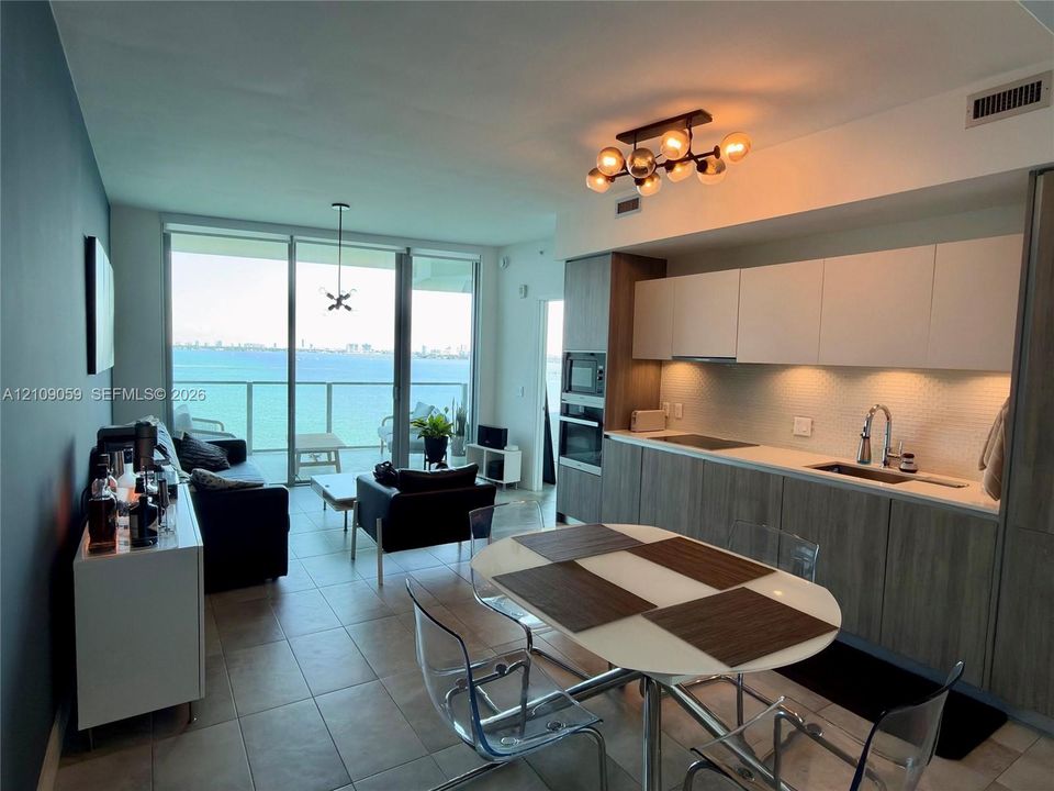 Open-concept interior featuring floor-to-ceiling glass doors, built-in cabinetry with matte finish, tile flooring, integrated kitchen appliances, and multi-globe ceiling lighting