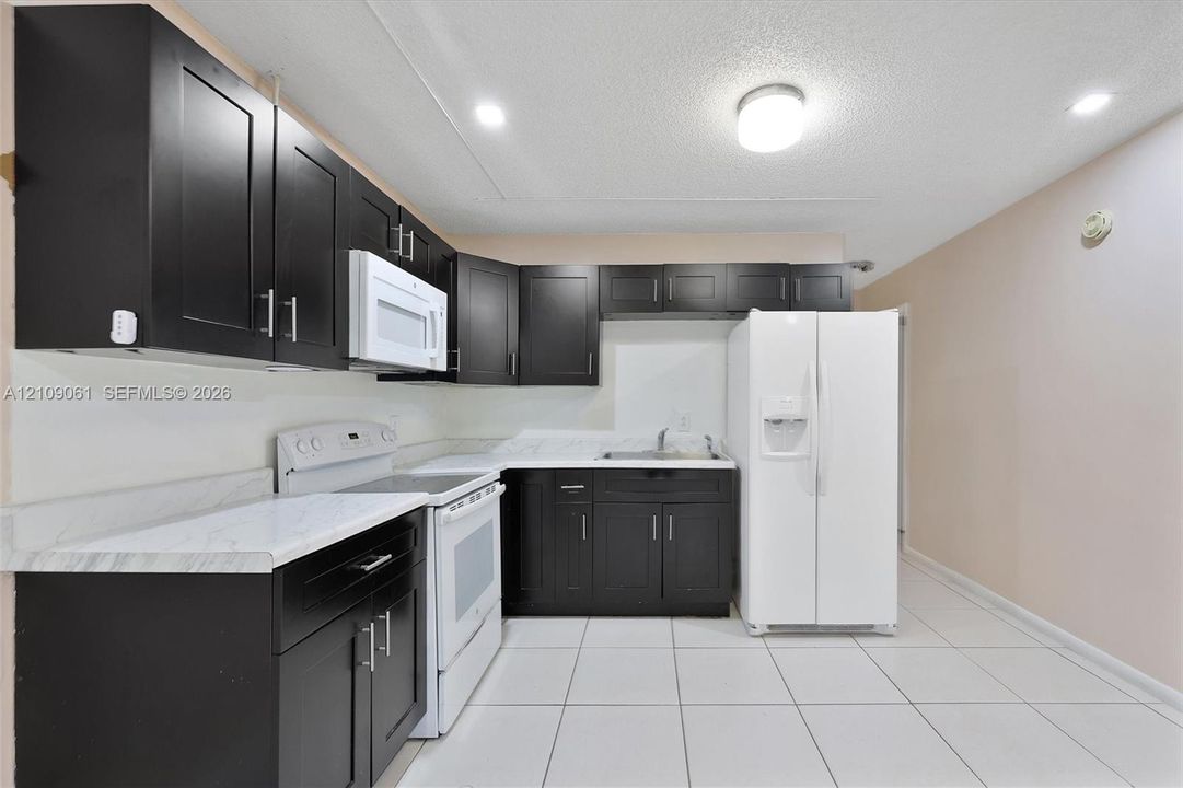 Kitchen featuring dark wood-finish cabinetry, white countertops, a built-in microwave, a side-by-side refrigerator, and tiled flooring