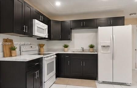Kitchen featuring dark shaker-style cabinetry, white countertops, a dual-basin stainless steel sink, and white appliances