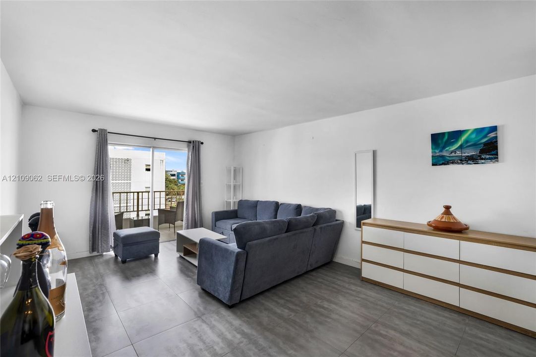 Living area featuring gray tile flooring, sliding glass doors to a balcony, and white walls