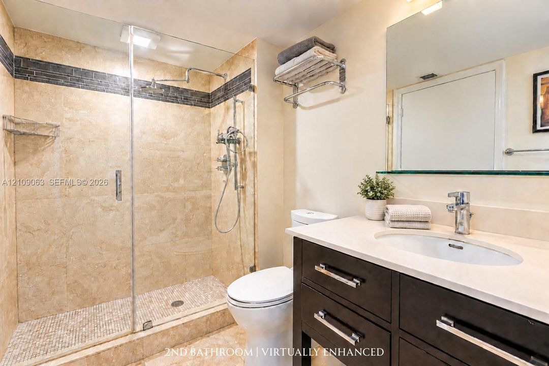 Bathroom featuring a walk-in shower with stone tile surround, pebble-style floor, and glass enclosure, complemented by a dark-finish vanity with a light-tone countertop and polished chrome fixtures