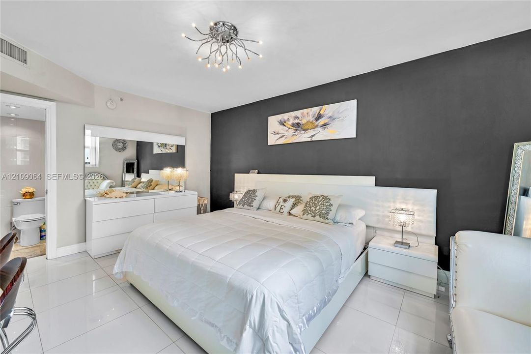 Sleeping area featuring high-gloss white built-in cabinetry, polished tile flooring, a charcoal accent wall, and a contemporary multi-arm chrome chandelier