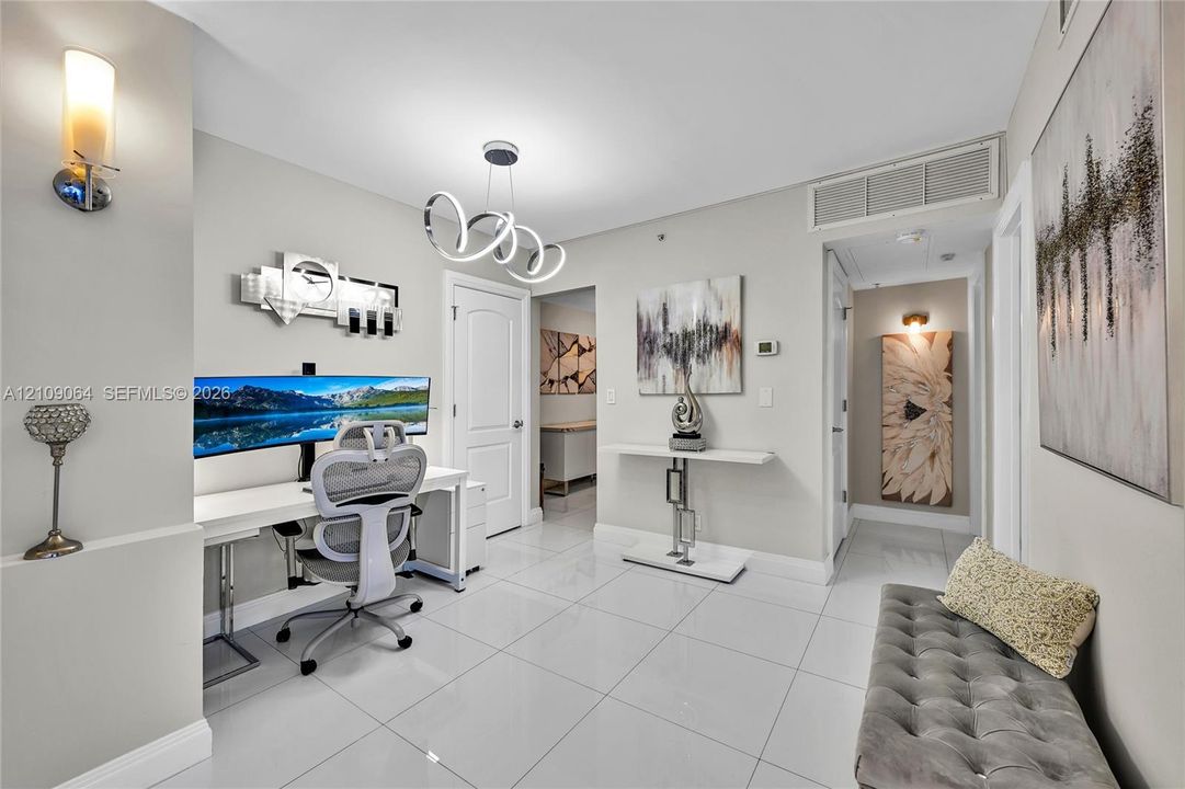 Open-concept space featuring polished tile flooring, a modern multi-ring sculptural chandelier, wall-mounted ambient sconce lighting, and a built-in recessed storage niche