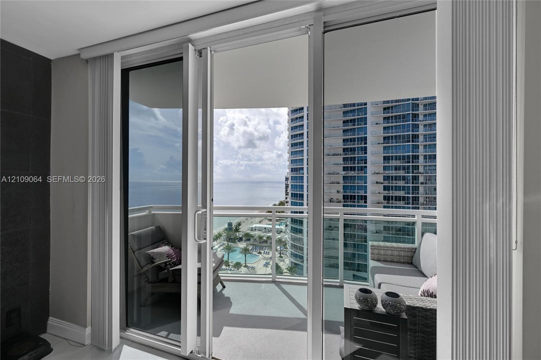Floor-to-ceiling sliding glass door system, balcony with white metal railing, and ocean horizon backdrop