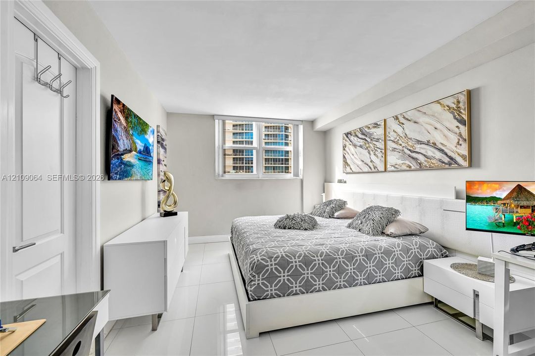 Neutral-toned interior featuring large-format tile flooring, a multi-panel window, and a built-in recessed headboard wall panel