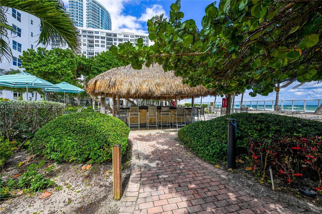 Outdoor bar featuring a thatched-roof structure, brick paver path, mature landscaping, and oceanfront proximity