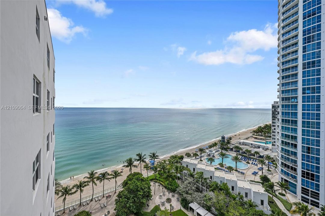 High-rise exterior featuring a glass curtain wall, expansive oceanfront scenery, a pristine sandy beach, and an outdoor swimming pool complex