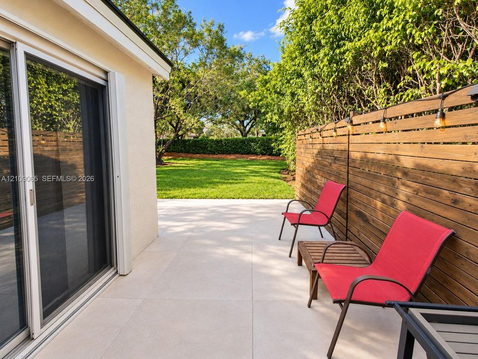 Backyard featuring large-format light-toned patio tiles, horizontal wood privacy fencing, and a manicured lawn