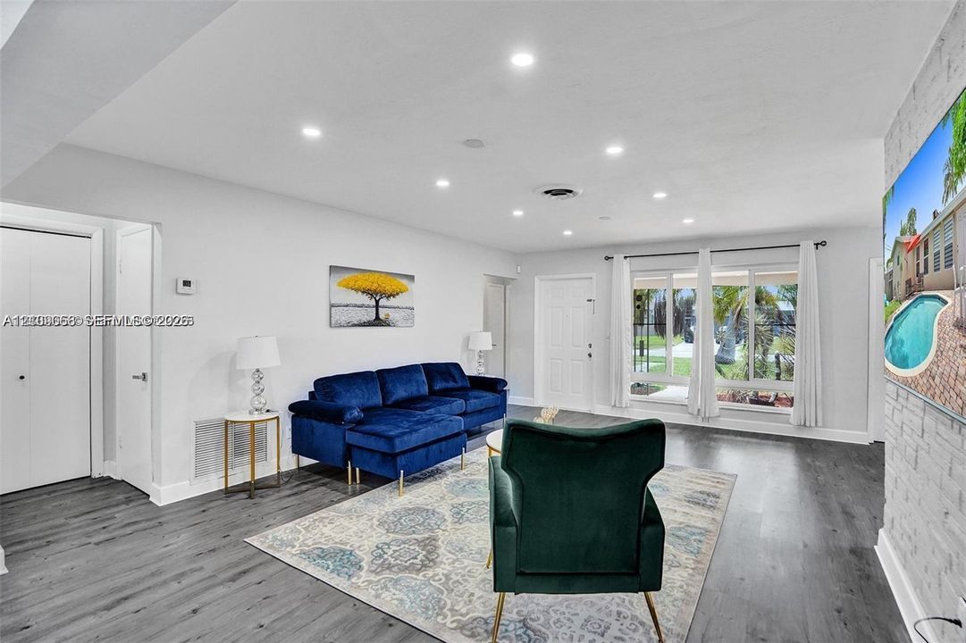 Open-concept living space featuring wood-finish flooring, recessed lighting, and a brick-texture accent wall