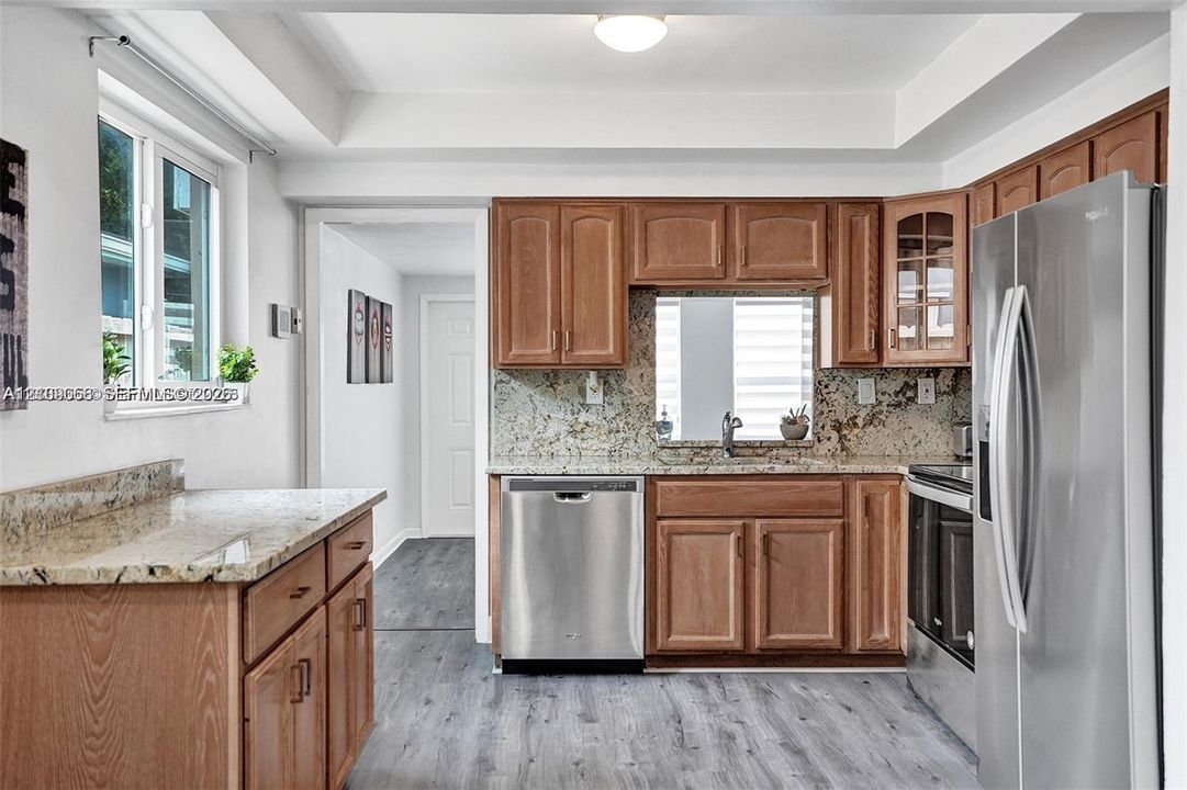 Kitchen featuring wood cabinetry, stone countertops, stainless steel appliances, and wood-finish flooring
