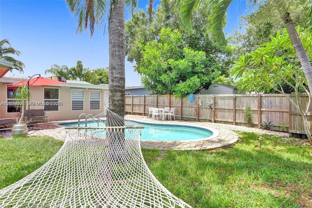In-ground swimming pool with stone-style paver decking, enclosed by a wood privacy fence and featuring mature palm trees