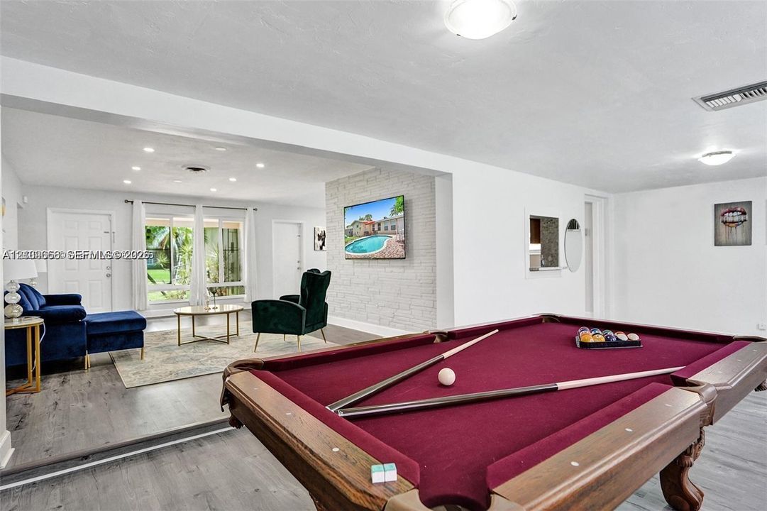 Open-concept living space featuring wood-finish flooring, a white-painted brick accent wall, recessed lighting, and expansive glass paneled exterior doors