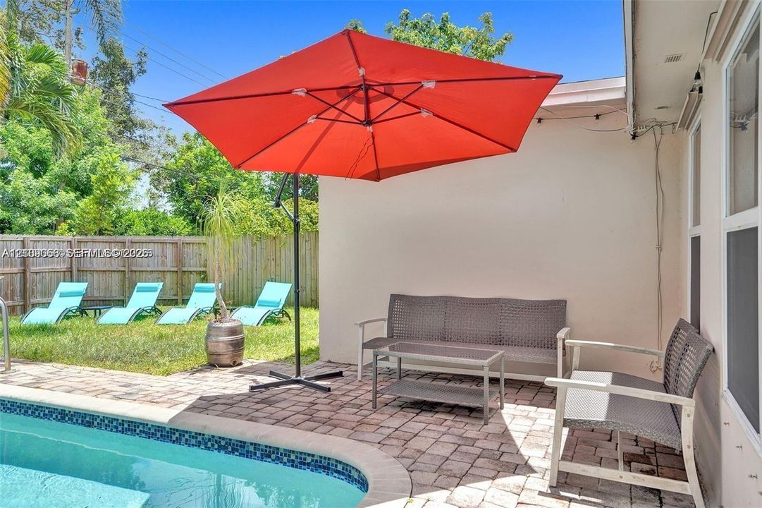 Backyard featuring a paver patio and a concrete-lined pool with a decorative tile border, enclosed by a wood privacy fence