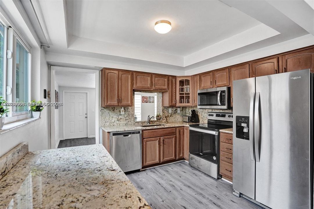 Kitchen featuring wood cabinetry, stone countertops, stainless steel appliances, and wood-finish flooring under a tray ceiling