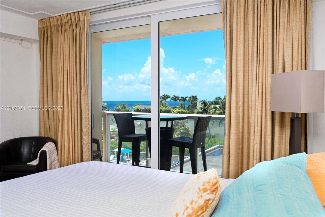 Sliding glass doors featuring floor-to-ceiling panels, metal-framed balcony with a glass railing, and an expansive ocean backdrop
