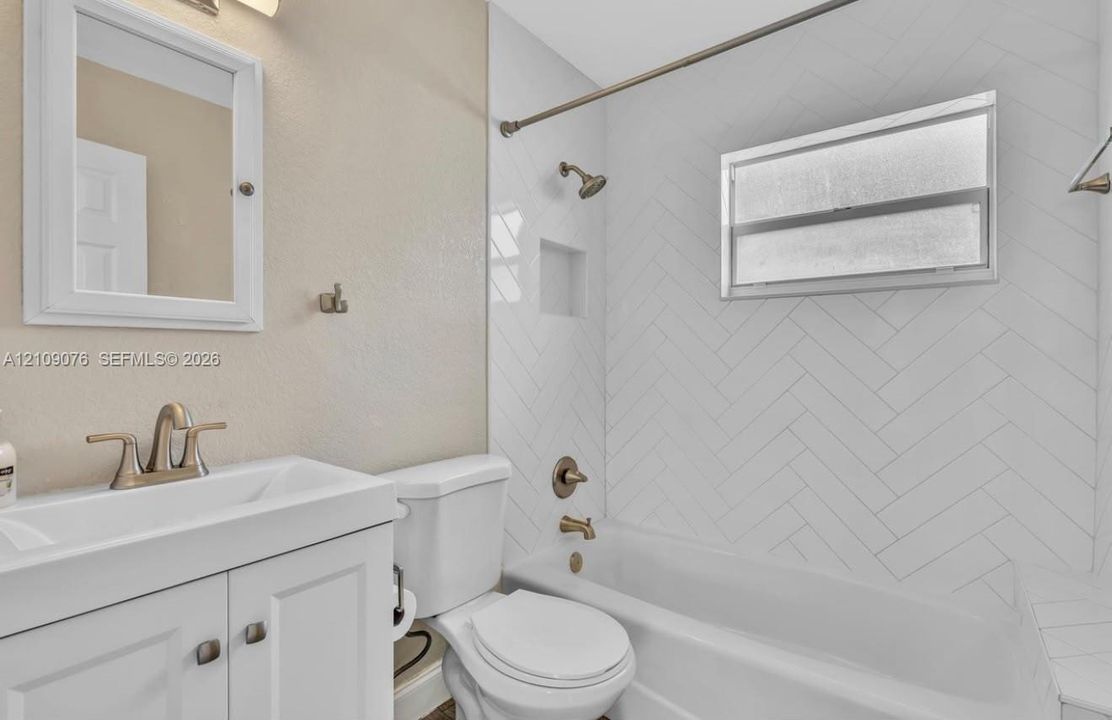 Bathroom featuring a white vanity cabinet, herringbone-patterned wall tile, built-in recessed wall niche, and metallic hardware finish