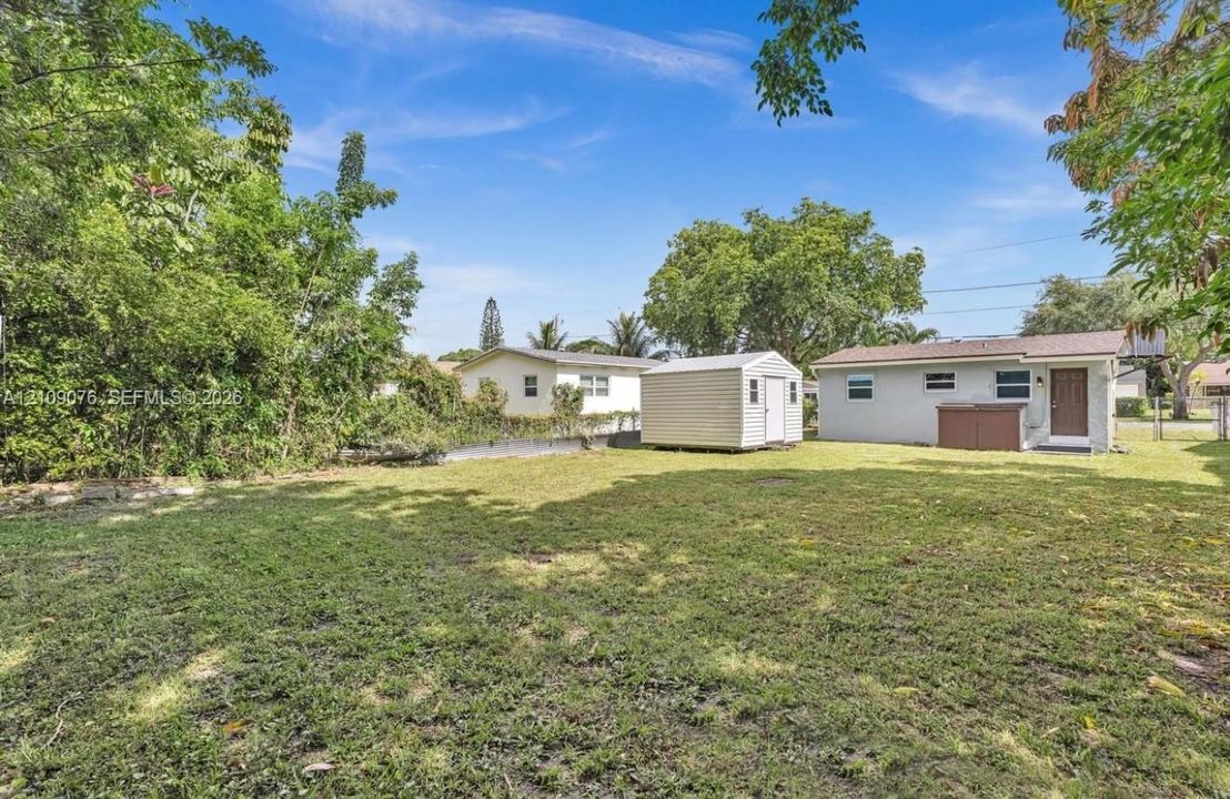 Expansive backyard featuring a level lawn, mature trees, a detached storage shed, and exterior access to the structure