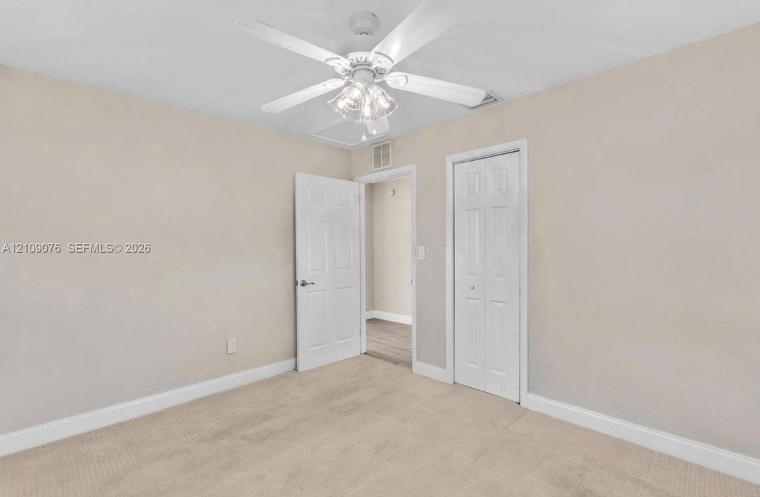 Neutral-toned carpeted flooring, white six-panel interior door, bi-fold closet door, and a white ceiling fan with integrated light fixture
