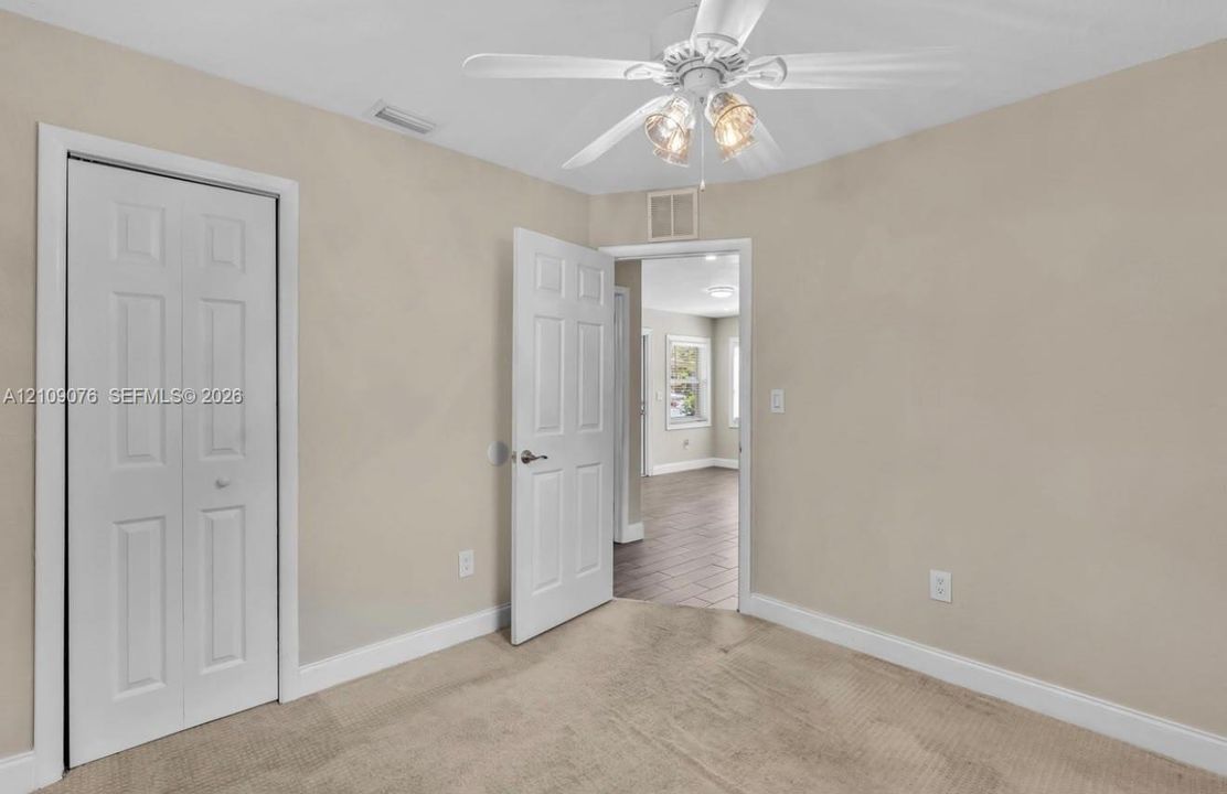 Neutral-toned interior space featuring carpeting, a white multi-panel door, a bi-fold closet door, and a ceiling fan with integrated lighting