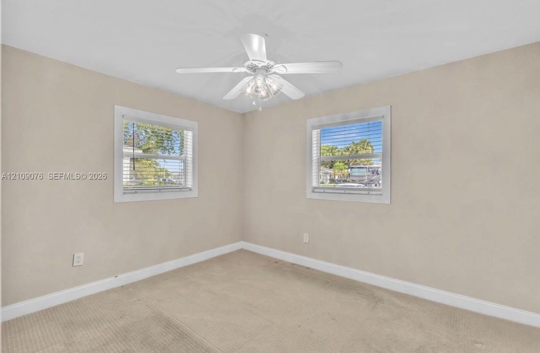 Neutral wall finish, carpeted flooring, two windows with horizontal blinds, and a white ceiling fan with integrated multi-bulb light fixture