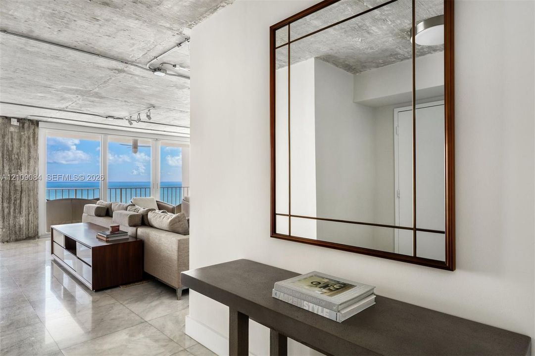 Exposed concrete ceiling, floor-to-ceiling glass paneling, stone-finish flooring, white flat-panel cabinetry, and a center island with a built-in wine refrigerator