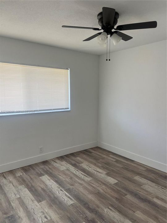 Room interior featuring wood-finish flooring, white walls, and a ceiling-mounted fan with integrated lighting