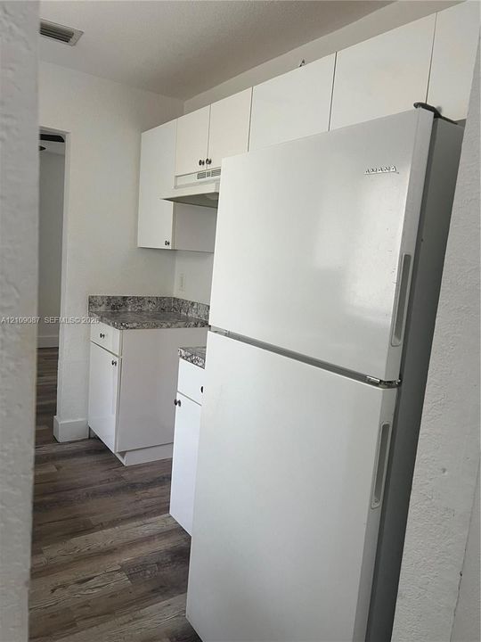 Kitchen featuring white shaker-style cabinetry, high-contrast patterned countertops, a top-freezer refrigerator, and wood-finish flooring