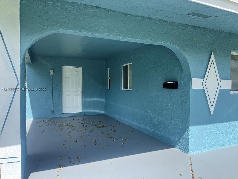 Covered entryway featuring a textured stucco exterior, architectural arched opening, diamond-shaped decorative trim, and solid-core door