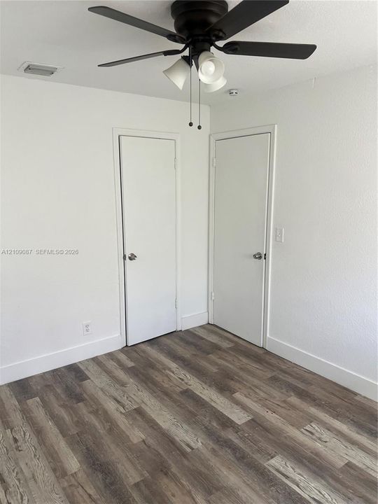 Wood-finish flooring, white walls, dual doors, and a ceiling-mounted fan with integrated lighting