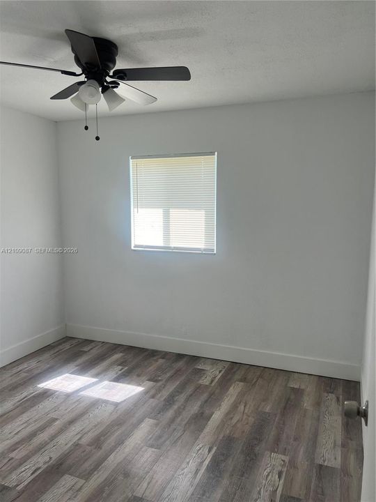 Interior room featuring wood-finish flooring, a matte black ceiling fan with integrated lighting, and a window with horizontal blinds
