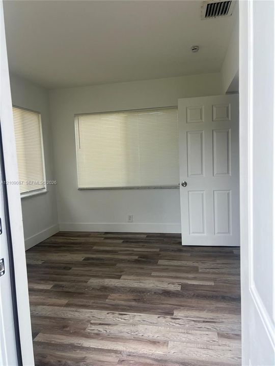 Room interior featuring wood-finish flooring, white walls, and a six-panel door