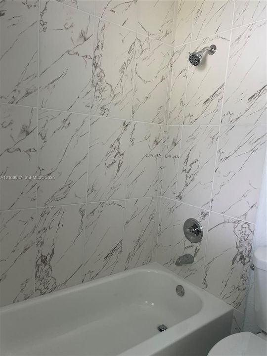 Bathtub surround featuring large-format veined tile, chrome shower head, matching chrome tub filler, and integrated pressure-balancing valve