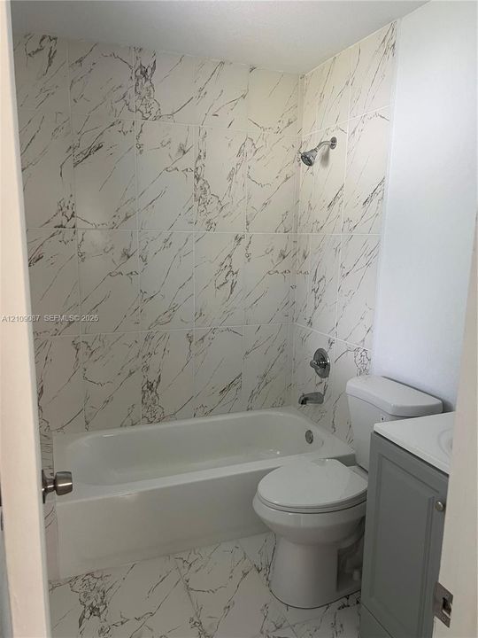 Bathroom featuring large-format tile flooring and wall surrounds with a veined pattern, built-in soaking tub, chrome fixtures, and a gray vanity cabinet