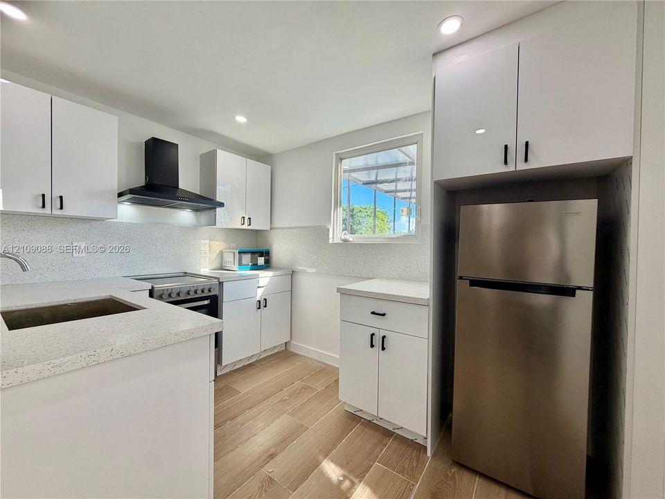 Kitchen featuring white shaker-style cabinetry, solid-surface countertops, a stainless steel refrigerator, and a matte black range hood