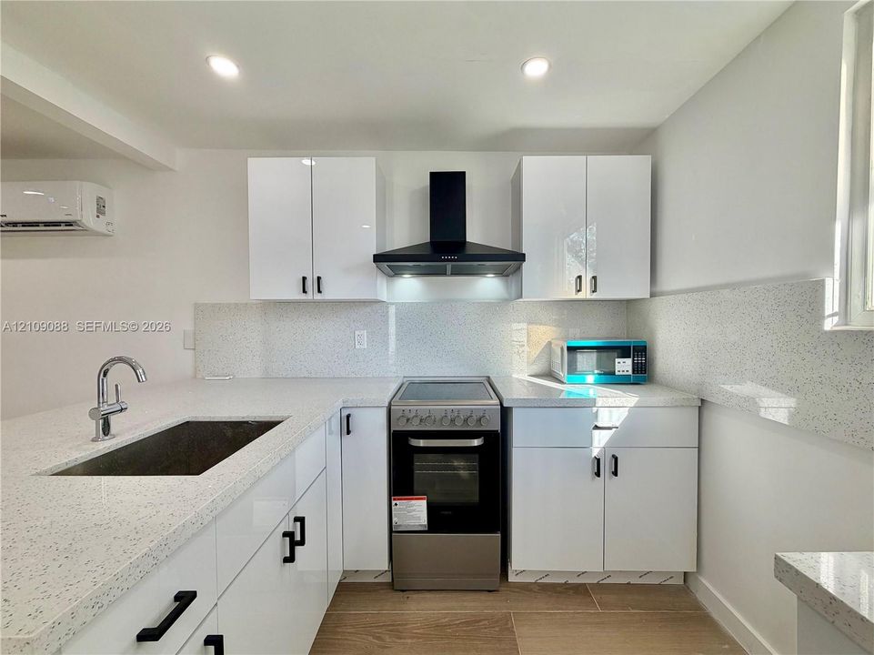 Kitchen featuring high-gloss white cabinetry, speckled stone-finish countertops, stainless steel range, matte black hardware, and wood-finish tile flooring