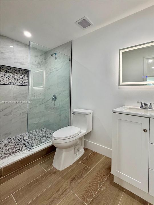 Walk-in shower with stone tile flooring, built-in niche, and glass enclosure
