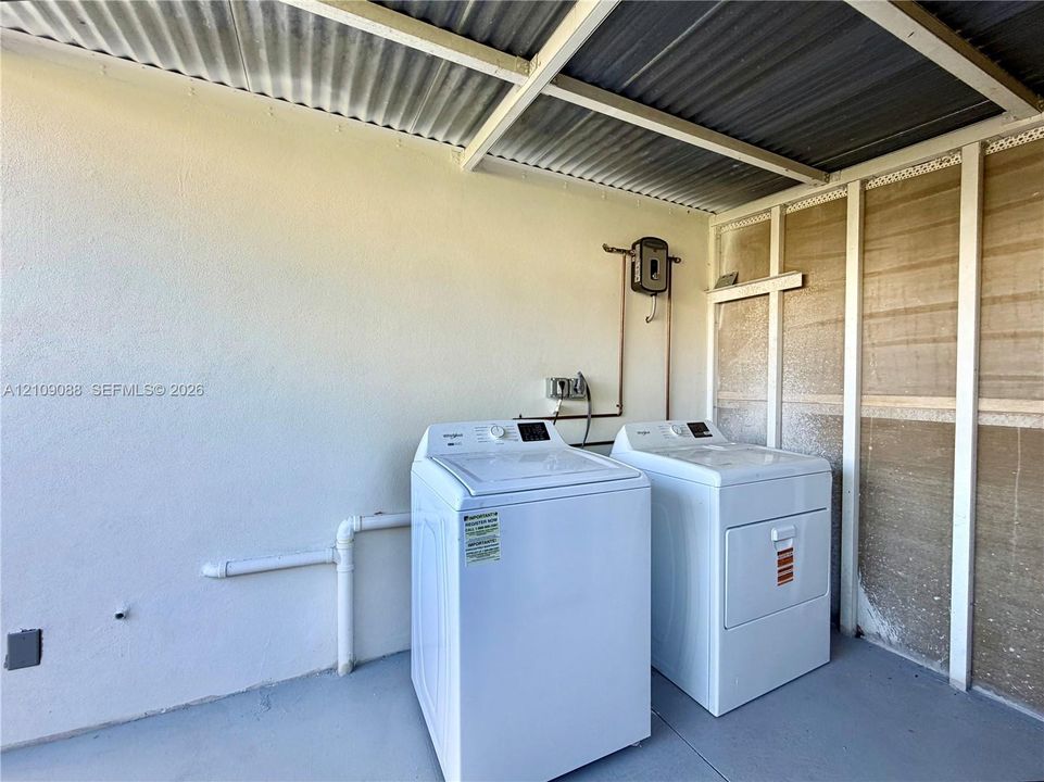 Covered laundry area featuring a corrugated metal roof, concrete flooring, and exposed structural framework