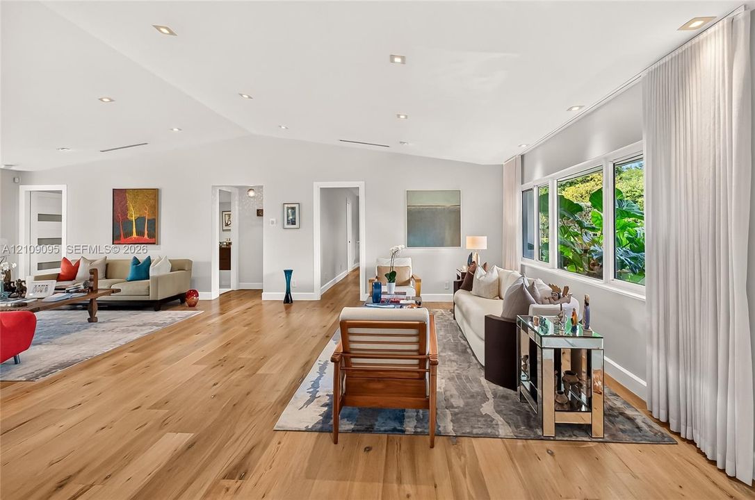 Open-concept living space featuring vaulted ceilings, wood-finish flooring, recessed lighting, and expansive windows