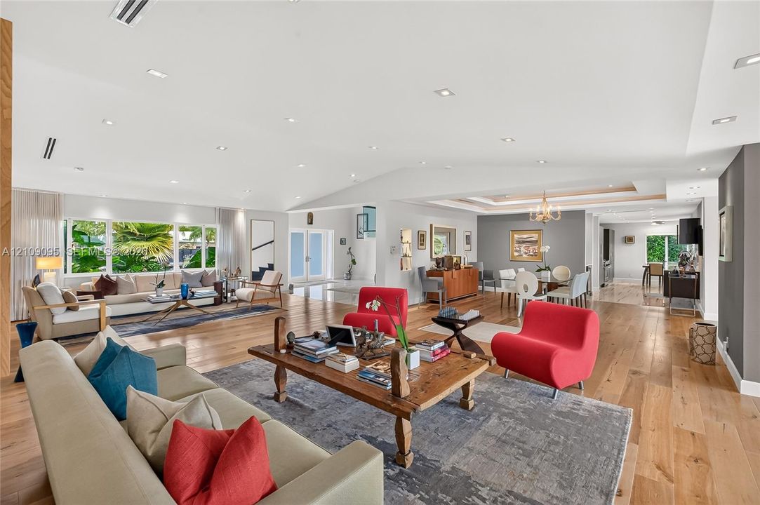 Open-concept living space featuring wood-finish flooring, vaulted ceilings, recessed lighting, and expansive window arrays