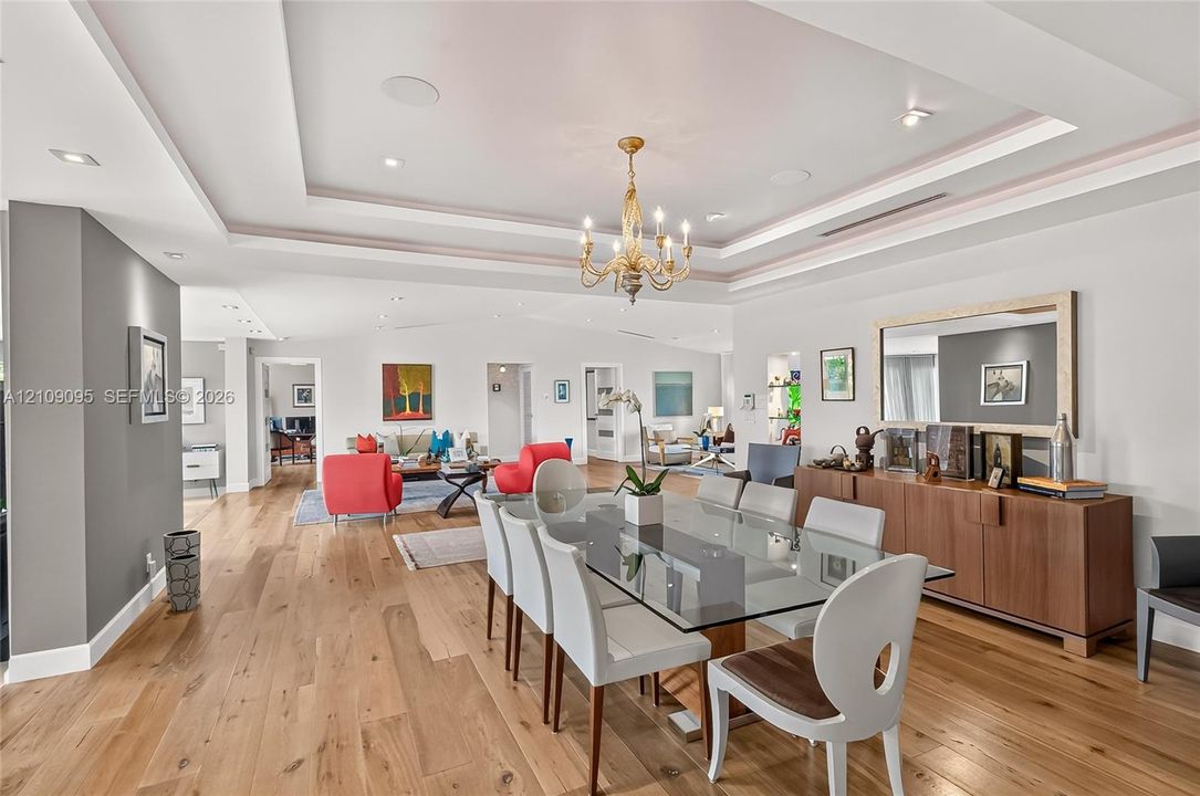 Open floor plan featuring wood-finish flooring, recessed lighting, multi-tiered tray ceiling, and a traditional six-arm chandelier