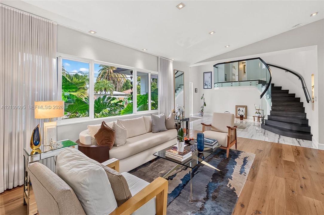 Vaulted ceilings with recessed lighting, floor-to-ceiling windows, wood-finish flooring, and a contemporary staircase with glass railing and dark wood treads