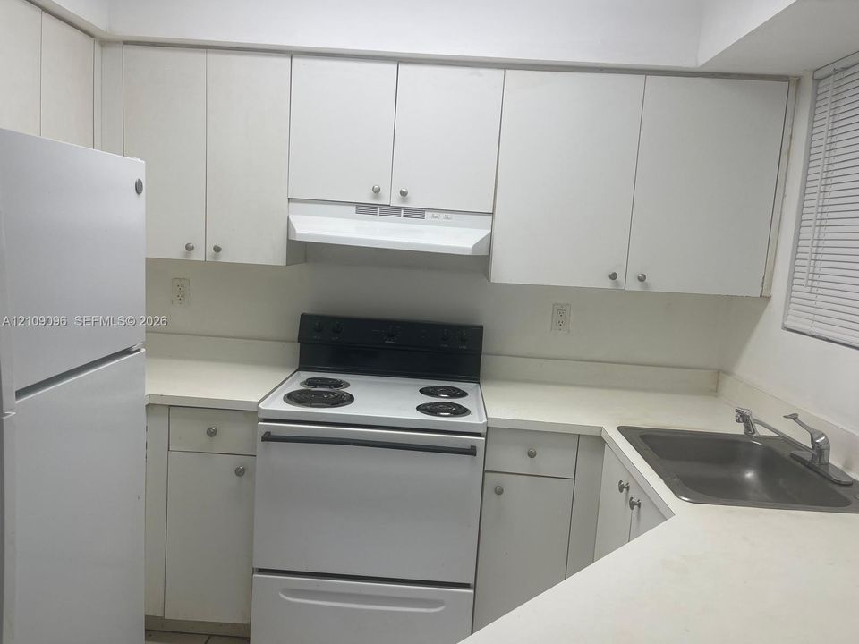 Kitchen featuring white cabinetry, integrated white refrigerator, electric range, coordinating white countertops, and a dual-basin stainless steel sink