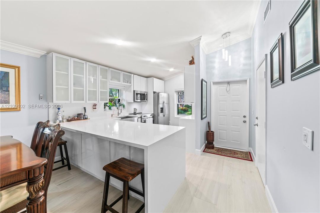 Kitchen featuring a white peninsula with a solid surface countertop, glass-front cabinetry, vaulted ceilings, and light-toned wood-finish flooring