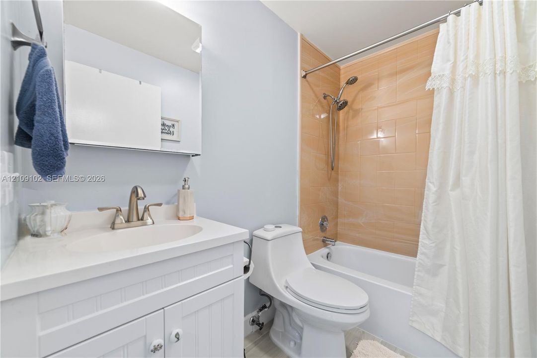 Bathroom featuring a white beadboard vanity with a solid-surface countertop, an integrated sink, a medicine cabinet, a dual-flush toilet, and a bathtub with a polished metallic shower fixture and light-toned tile surround