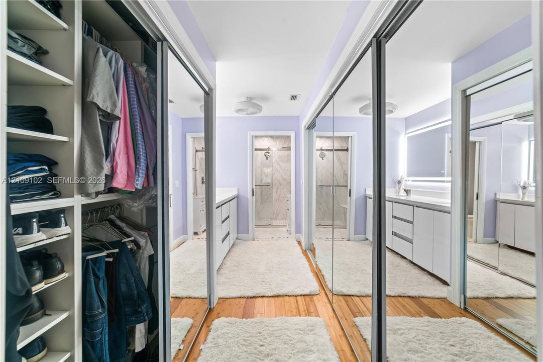 Walk-in closet featuring floor-to-ceiling custom shelving, dual-sided mirrored sliding doors, wood-finish flooring, and recessed ceiling lighting