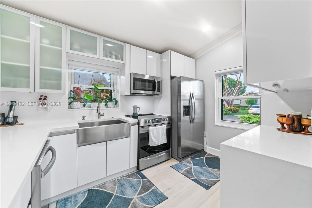 Kitchen featuring white flat-panel cabinetry with glass-front uppers, stainless steel apron-front sink, stone-finish countertops, and matching stainless steel appliances